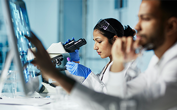 male researcher looking at computer screen and female researcher looking at microscope